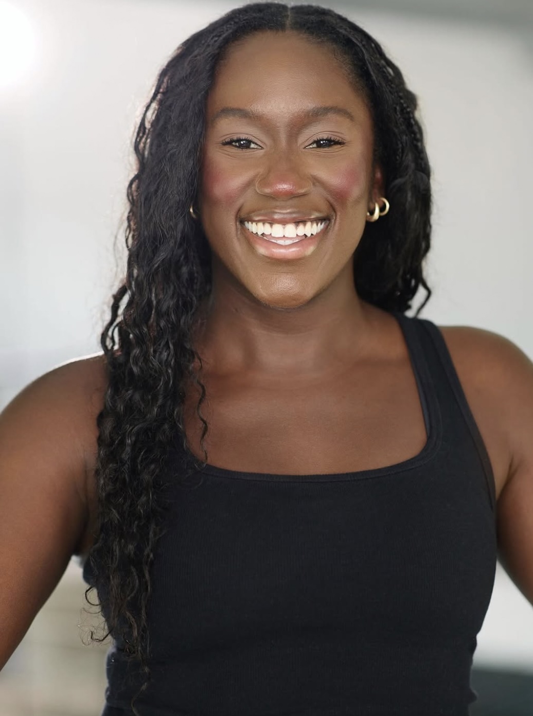 Portrait of Niyah smiling, with long curly hair and a black tank top